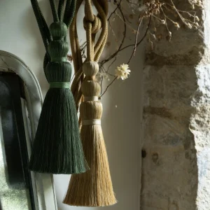 Assorted curtain tieback tassels in green, brown, and beige hanging in natural light