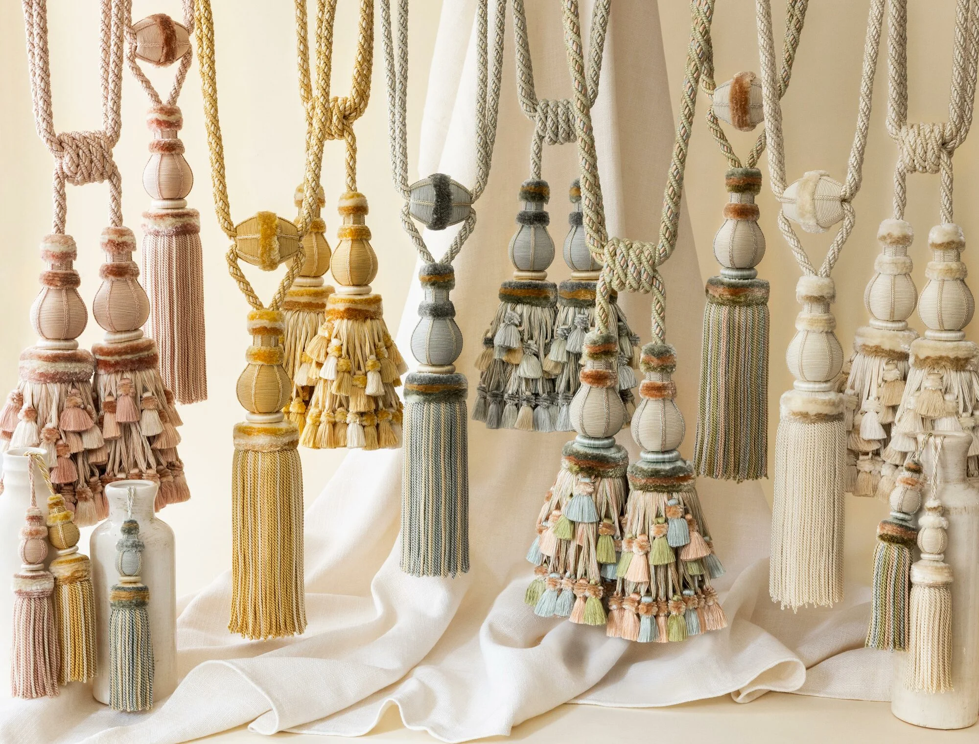 Assorted handcrafted curtain tiebacks with decorative tassels in pastel and earthy tones, displayed elegantly on a neutral fabric background – showcasing traditional Indian craftsmanship and detailed textile artistry.